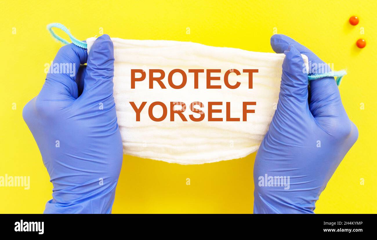 Medizinische Maske mit dem Text Protect yourself Arzt hält Handschuhe auf gelbem Hintergrund Stockfoto
