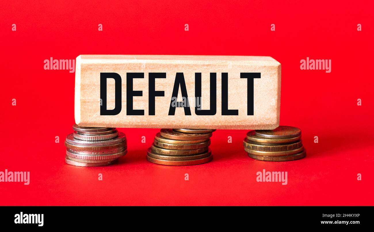Das Wort DEFAULT steht auf einem Holzblock, der auf Münzen und einem roten Hintergrund steht. Konzept zur Erhöhung der Verschuldung. Stockfoto