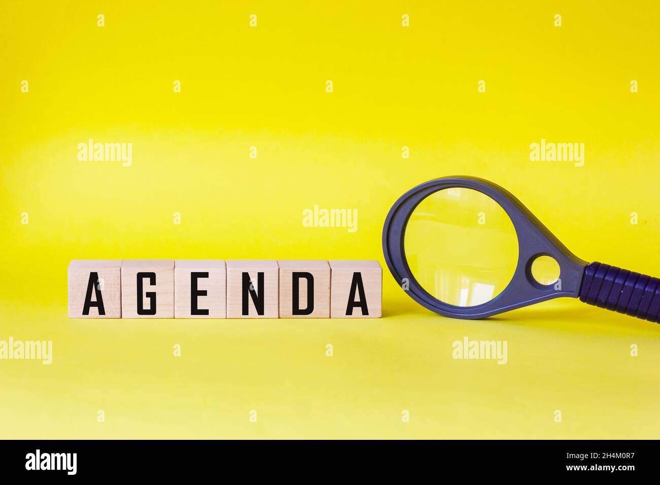 Agenda - Wörter aus Holzblöcken mit Buchstaben, Liste der Tagesordnungspunkte Konzept, auf gelbem Hintergrund Lupe Stockfoto