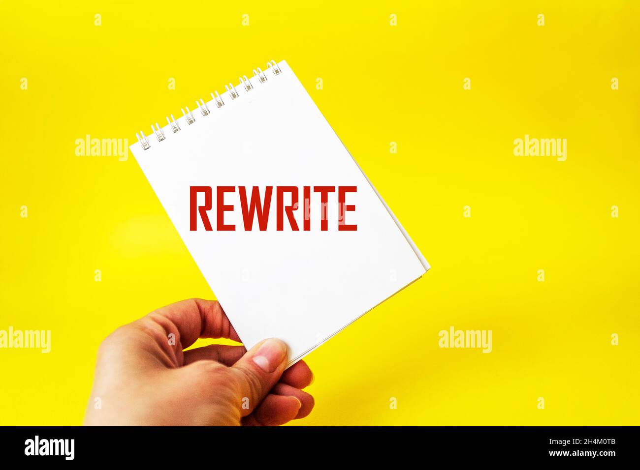 Das Wort rewrite auf einem Notizbuch in einer weiblichen Hand und einem gelben Hintergrund Stockfoto