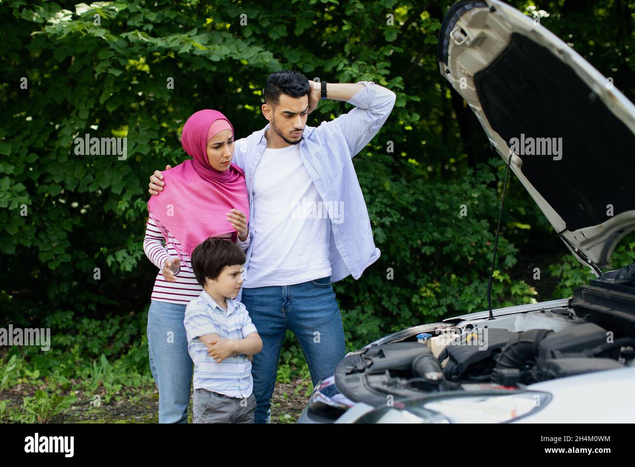 Verwirrte Muslimische Familie Mit Kleinem Sohn, Der In Der Nähe Von Kaputten Autos Im Freien Steht, Verärgerte Eltern Aus Dem Nahen Osten Und Männliche Kinder, Die Probleme Mit Ihrem Ve Stockfoto