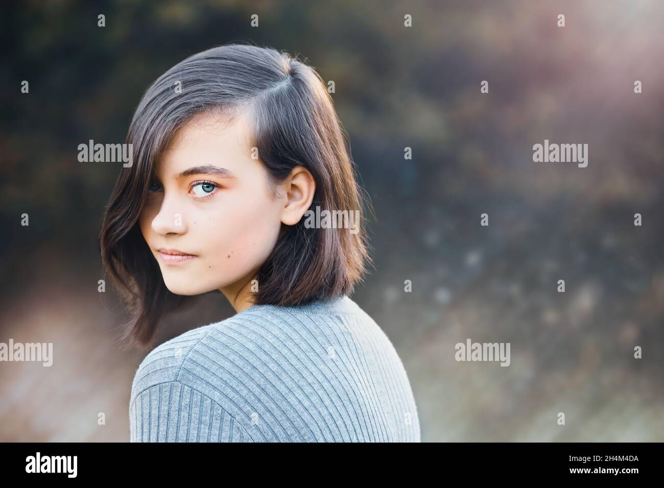 Content glücklich Teenager-Mädchen posiert Blick auf Kamera über ihre Schulter. Streulicht mit verschwommenem Herbsthintergrund. Stockfoto