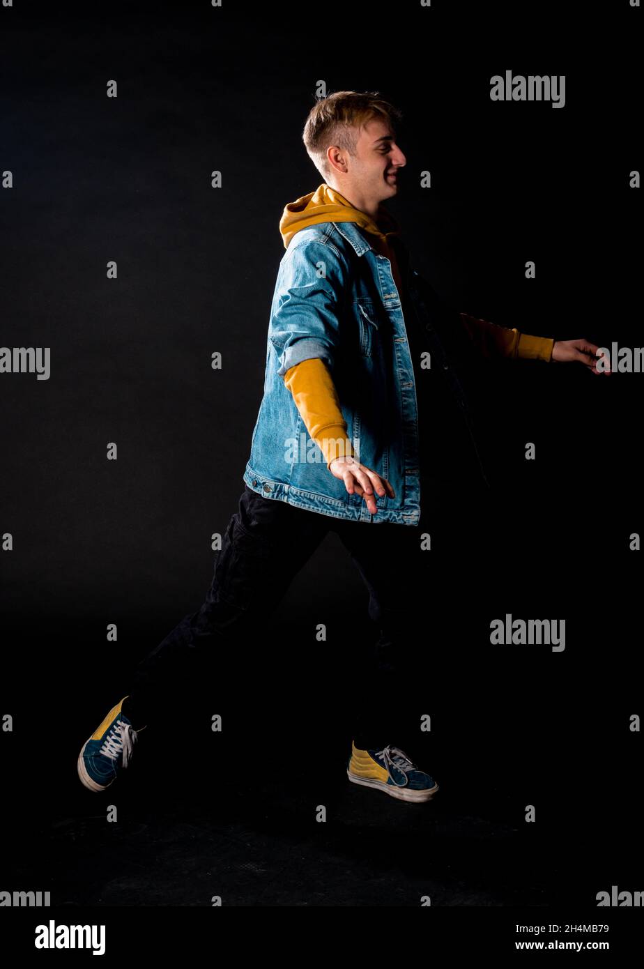 Cooler junger Mann in blauer Jacke, der im modernen Studio vor schwarzem Hintergrund posiert Stockfoto