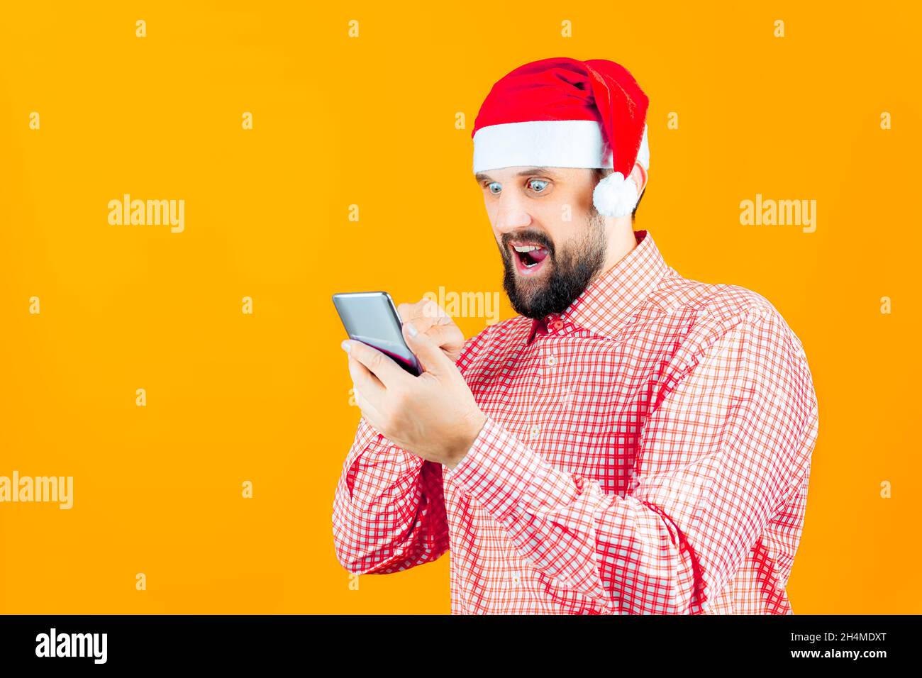 Bärtiger Mann mit Weihnachtshut der Weihnachtsmann schaut ins Telefon Stockfoto