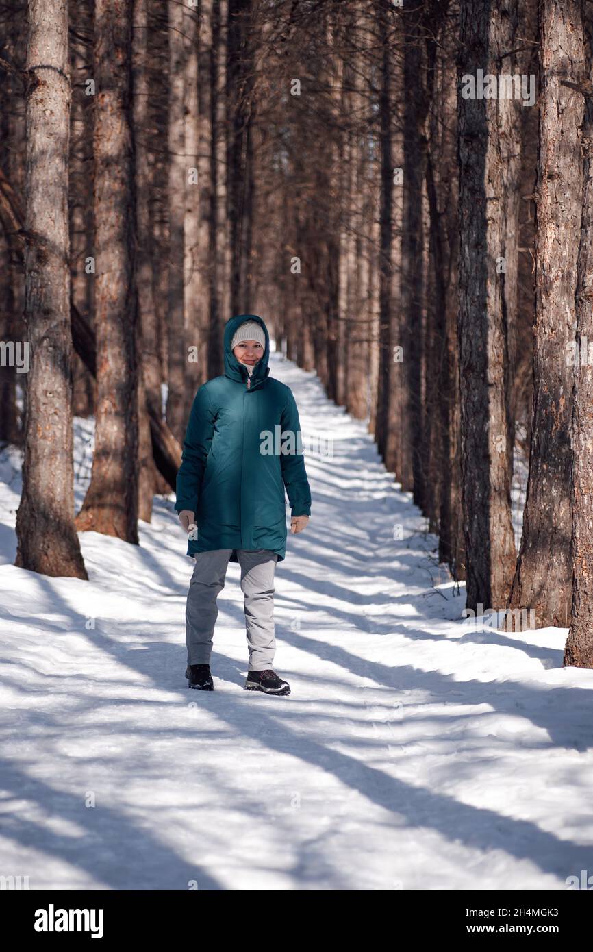 Kaukasische Frau, die im Wald läuft. Junge attraktive Frau in warmer Daunenjacke steht auf schneebedeckter Straße nach dem Schneesturm und genießt die Sonne auf frostigen Stockfoto