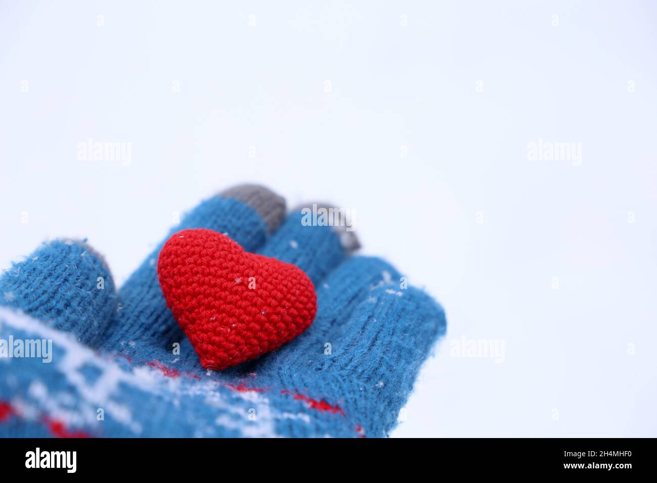 Rotes Herz auf der Handfläche im warmen Strickhandschuh gegen den Schnee. Konzept einer romantischen Liebe, Valentinstag oder Nächstenliebe Stockfoto