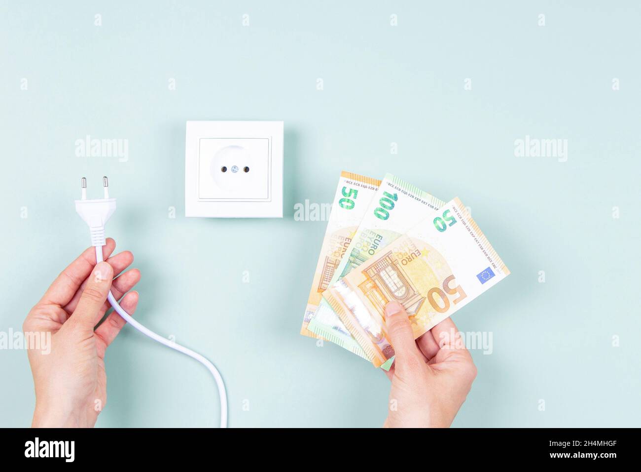 Stromkosten und teures Energiekonzept. Weibliche Hände mit einem elektrischen Stecker und Euro-Geldscheinen in der Nähe einer weißen Steckdose auf dem Licht Stockfoto