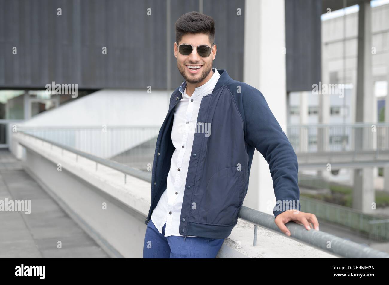 In der modernen Innenstadt steht ein junger, zwangloser Mann, der die Kamera anschaut und eine Sonnenbrille trägt. Hochwertige Fotos. Stockfoto