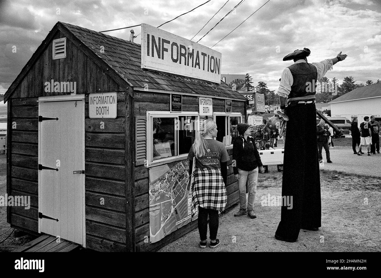 Ein Riese, der eine mase, ein Schwert und eine Axt trägt, weist zwei Frauen an einem Informationsstand auf der Deerfield Fair - Deerfield, New Hampshire, den Weg. Schwarz und Stockfoto