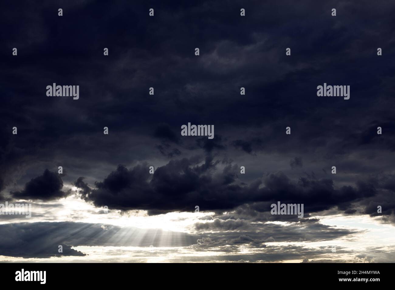 Schwarze Wolken mit Sonnenstrahlen. Dramatischer dunkler Himmel mit Sonnenlicht. Himmlisch Stockfoto