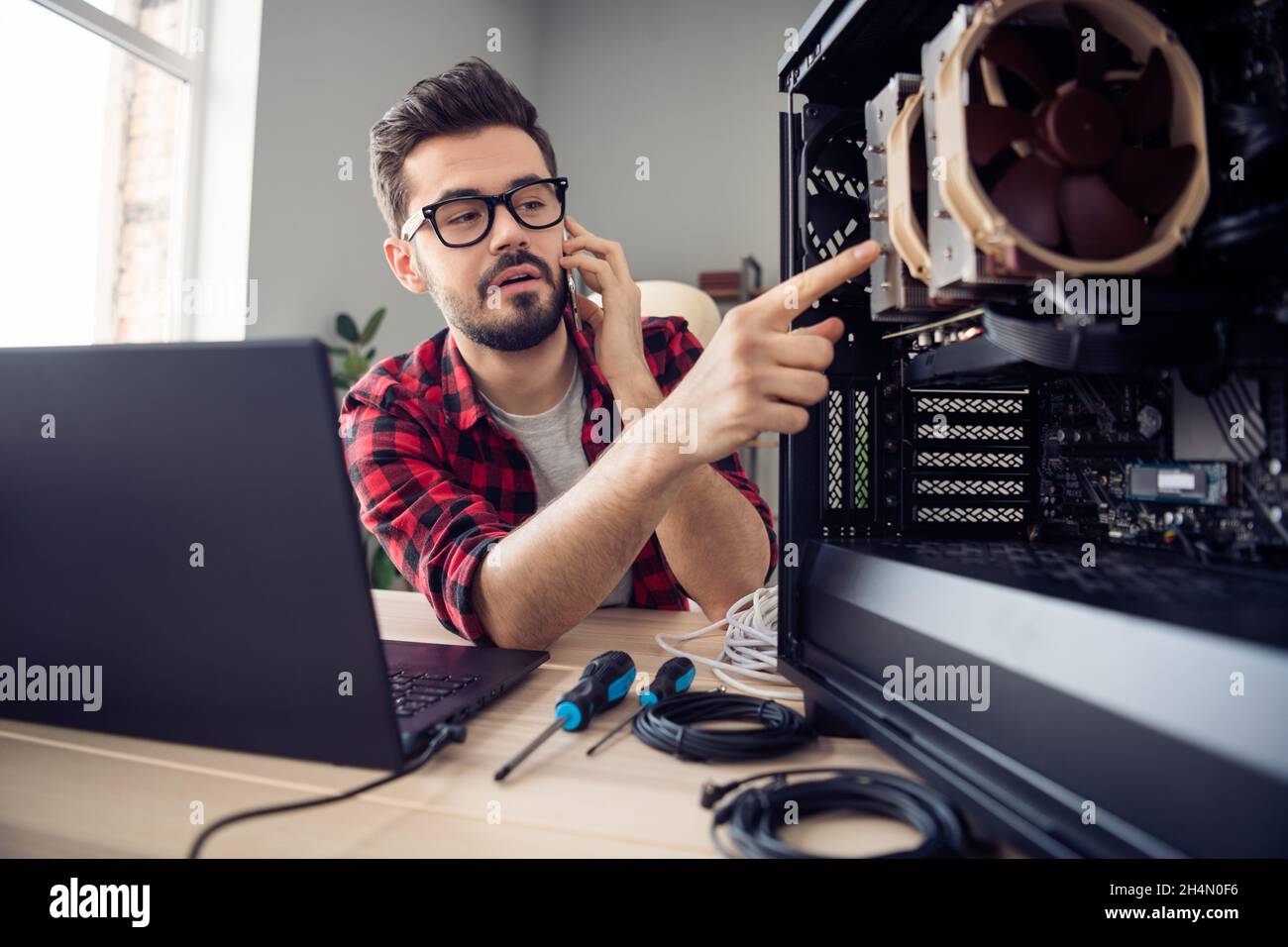 Porträt eines attraktiven, trendigen Mannes, der den Kunden kontaktiert, der den Motherboard-Prozessor auf der Workstation im Büro aufrüstet Stockfoto