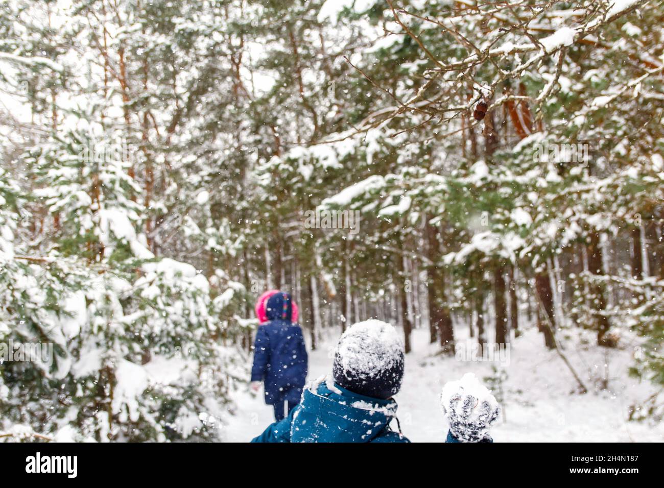 Der Junge wirft einen Schneeball auf das Mädchen. Lustige Kinder im Winter Park spielen Schneebälle und verbringen aktiv Zeit im Freien. Winter verschneiten Wald. Kalt f Stockfoto