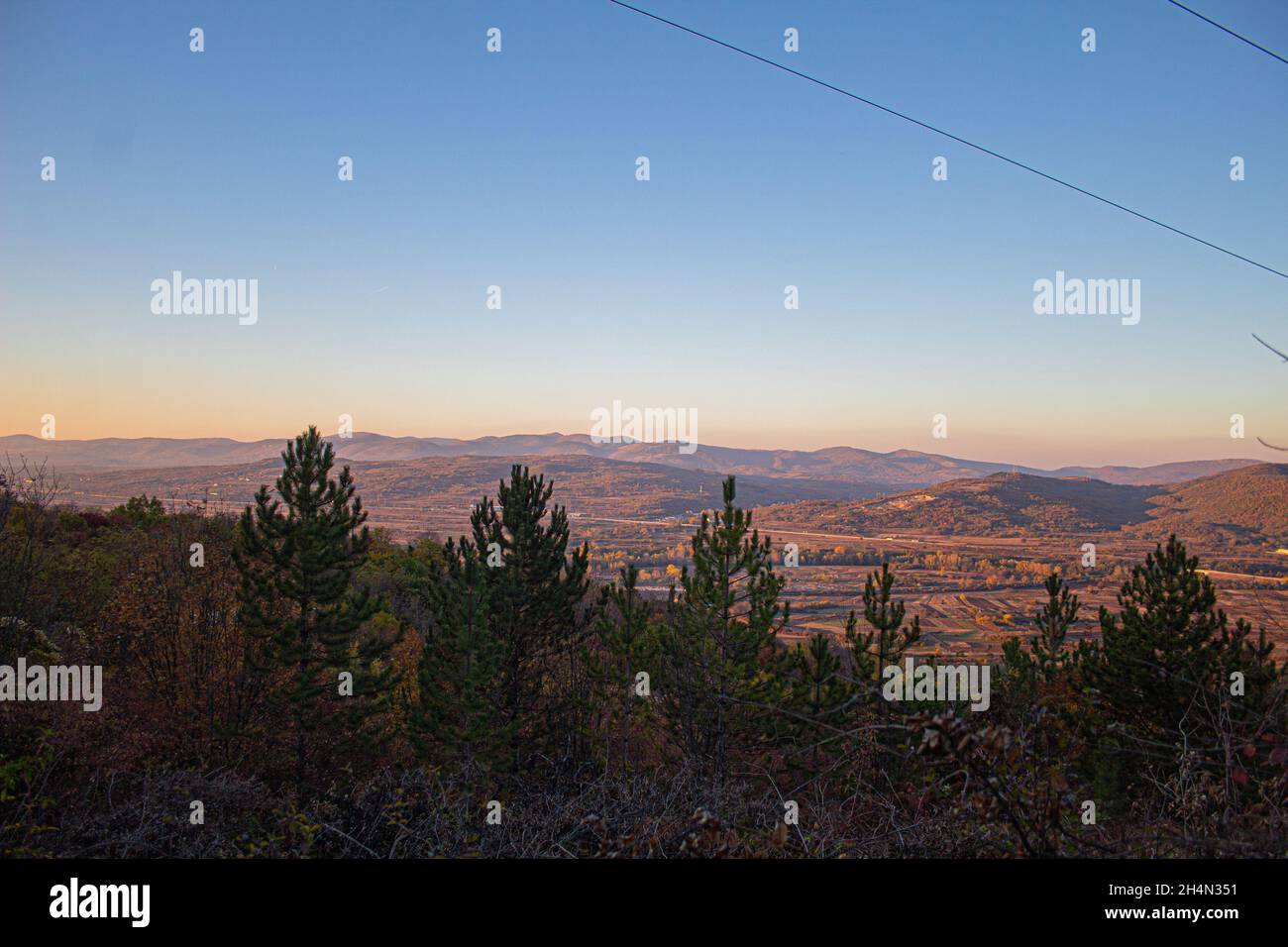 Blauer Himmel der Landschaft von Crni Kamen in Suva Planina Nis. Naturtapete ultra breite Natur mit Stadt in der Ferne, Felder und Bäume aufgenommen Stockfoto