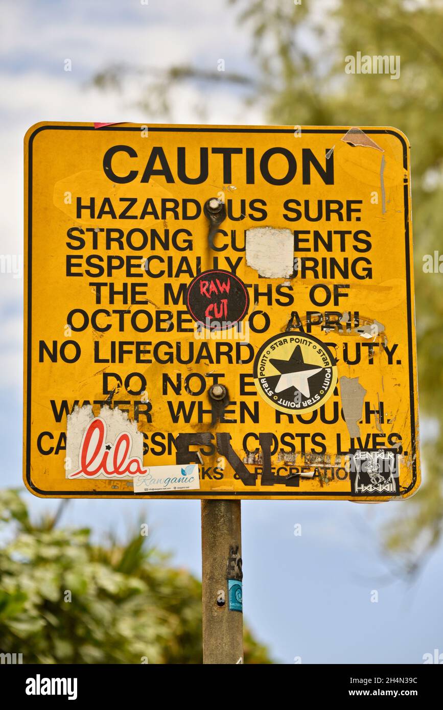 Graffiti, Stoßfänger-Aufkleber und andere Aufkleber, die über gefährlicher Brandung kleben und verputzen Vorsicht Gefahrenbrandzeichen auf Oahu, Hawaii, USA Stockfoto