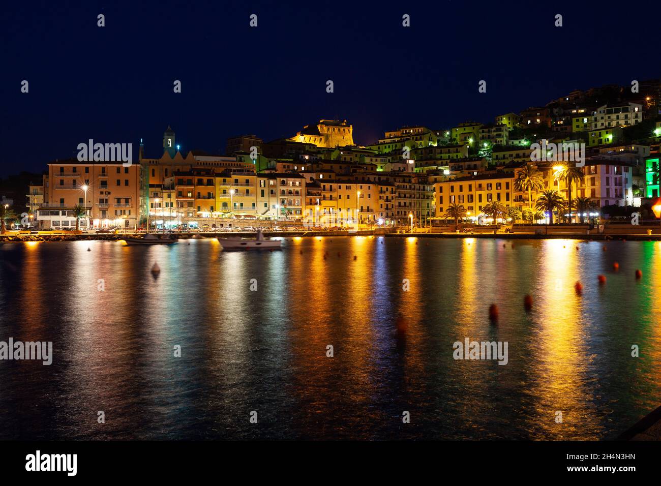 Kleine Stadt Porto Santo Stefano bei Nacht, Monte Argentario, Toskana, Italien, mit Stadtlichtern und Reflexionen auf dem Wasser Stockfoto