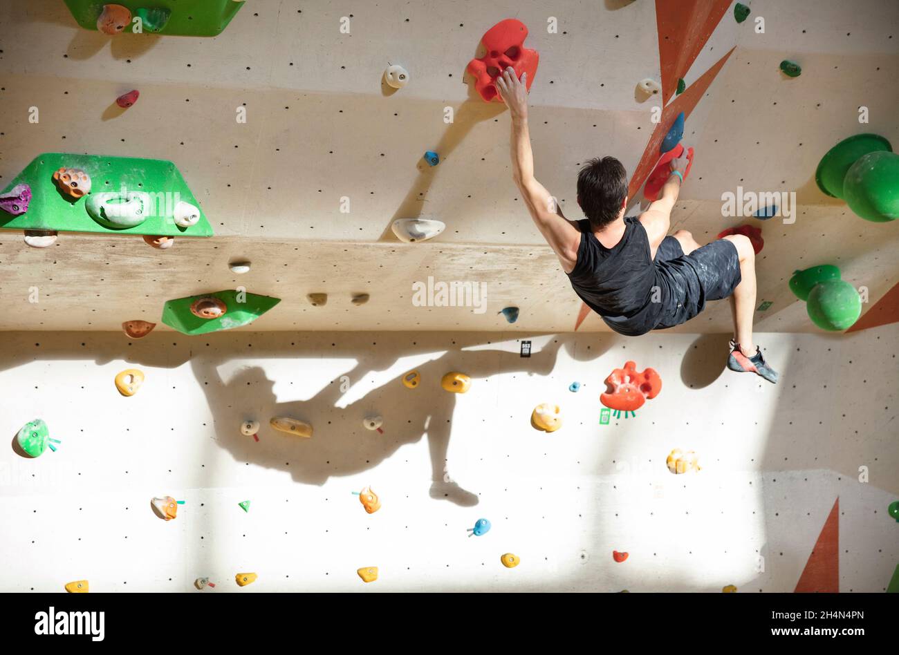 Kaukasischer junger Mann, der in einer Kletterhalle mit klarem Schatten an der Wand Bouldern kann Stockfoto
