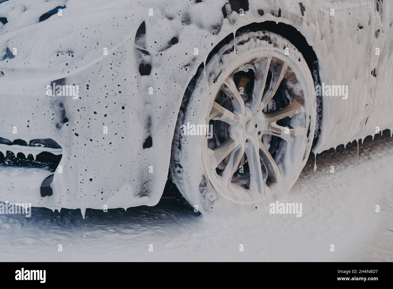 Autorad in weißem Seifenschaum an der Autowaschstation Stockfoto
