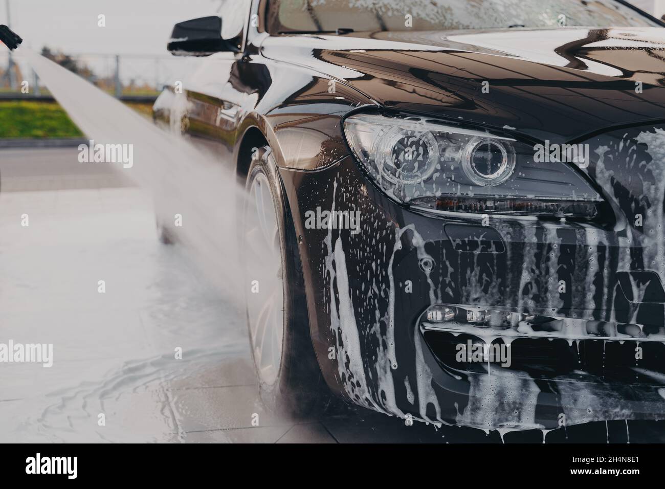 Professionelle Autowäsche, Sprühen von Wasser aus Hochdruckreiniger, um die Laugen abzuspülen Stockfoto