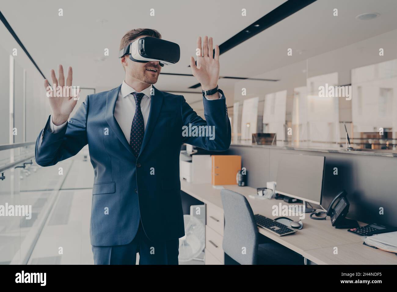 Geschäftsmann in einer Virtual-Reality-Brille, die neben dem Schreibtisch im Büro steht Stockfoto