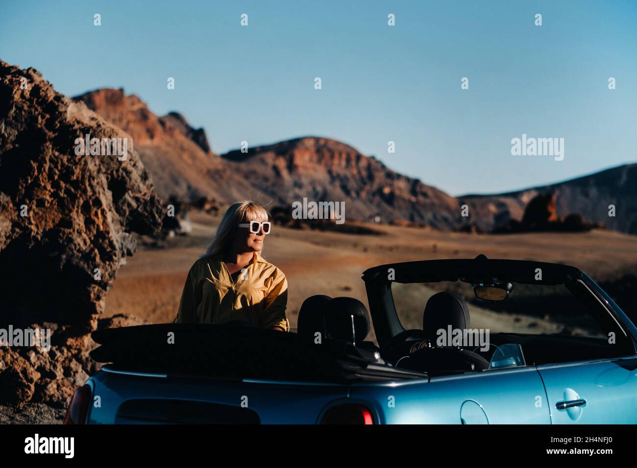 Frau, die auf der Straße unterwegs ist, steht mit Karte in der Nähe eines Cabrio-Wagens am Straßenrand im vulkanischen Bergwald auf der Insel Tenera, Spanien Stockfoto