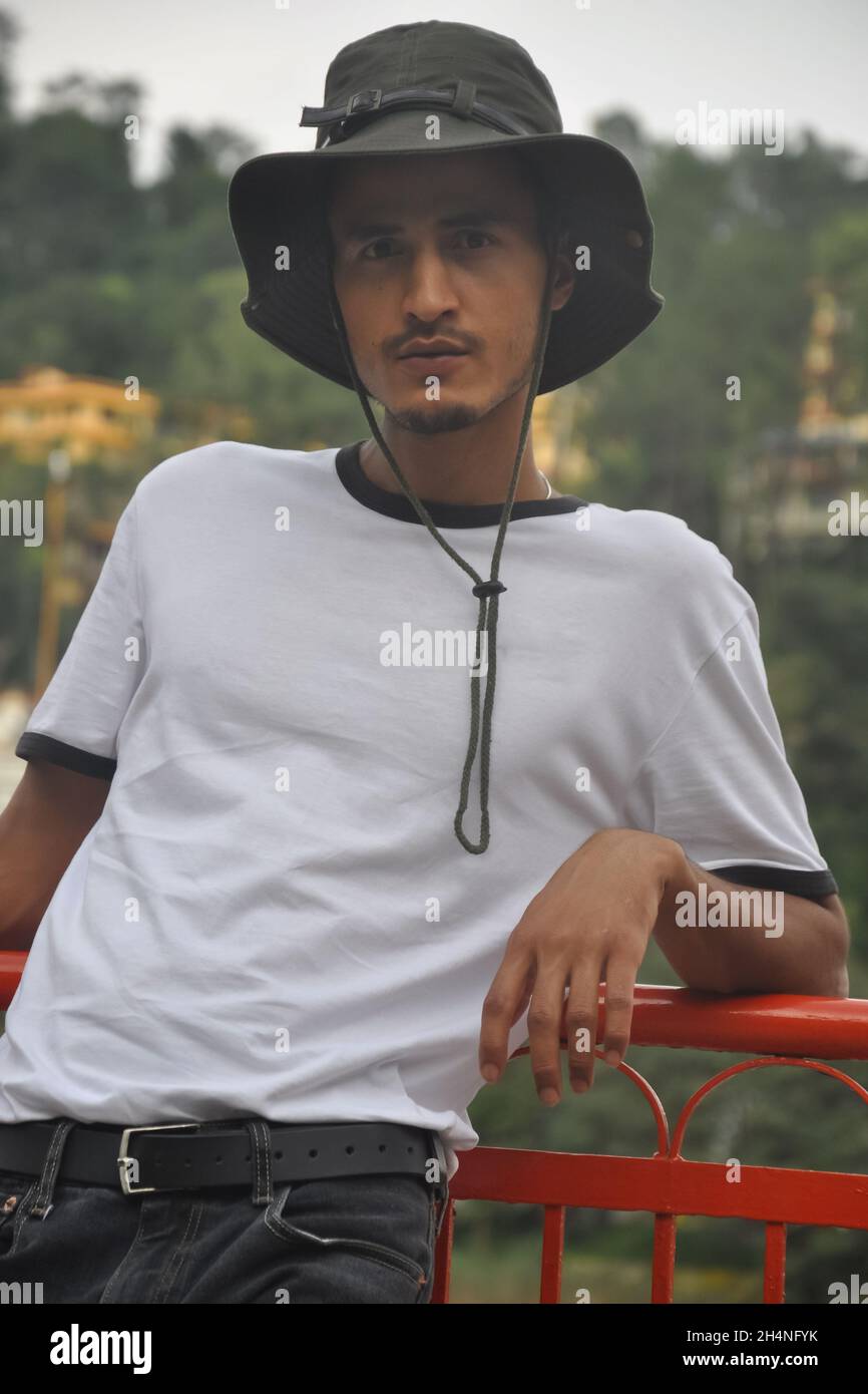 Ein junger Mann aus dem Norden Indiens posiert im Freien mit Boonie-Hut und weißem T-Shirt und blickt auf die Kamera Stockfoto