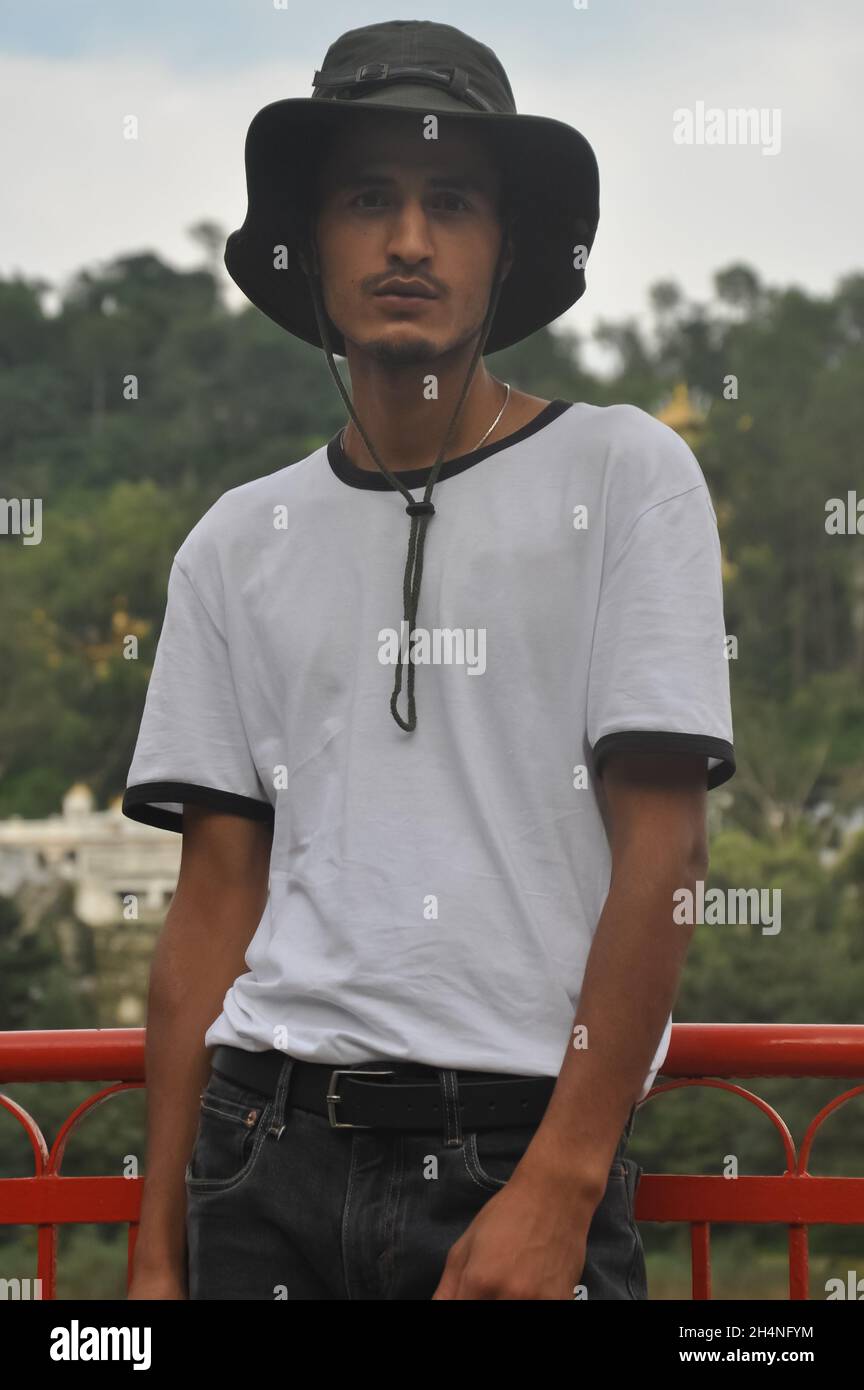 Ein junger Mann aus dem Norden Indiens posiert im Freien mit Boonie-Hut und weißem T-Shirt und blickt auf die Kamera Stockfoto