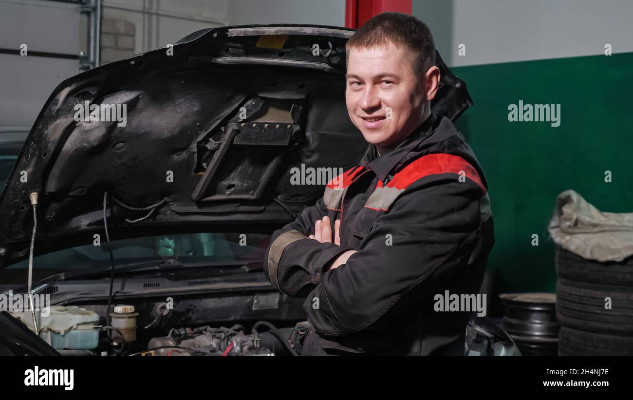 Techniker mit gekreuzten Armen steht bei einem renovierten Auto Stockfoto