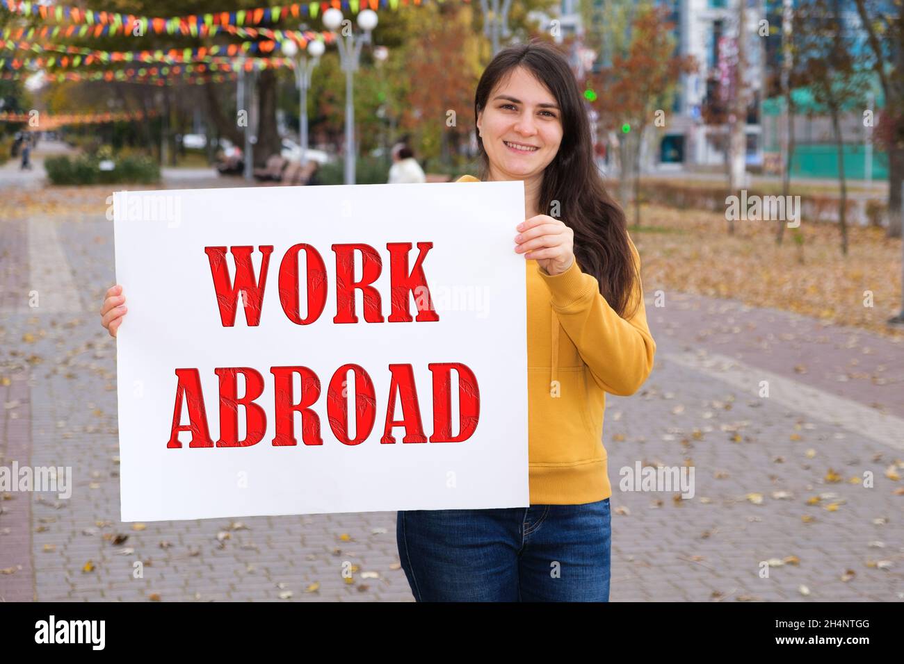 Eine Frau lächelt und hält ein Plakat mit der Textarbeit im Ausland Stockfoto