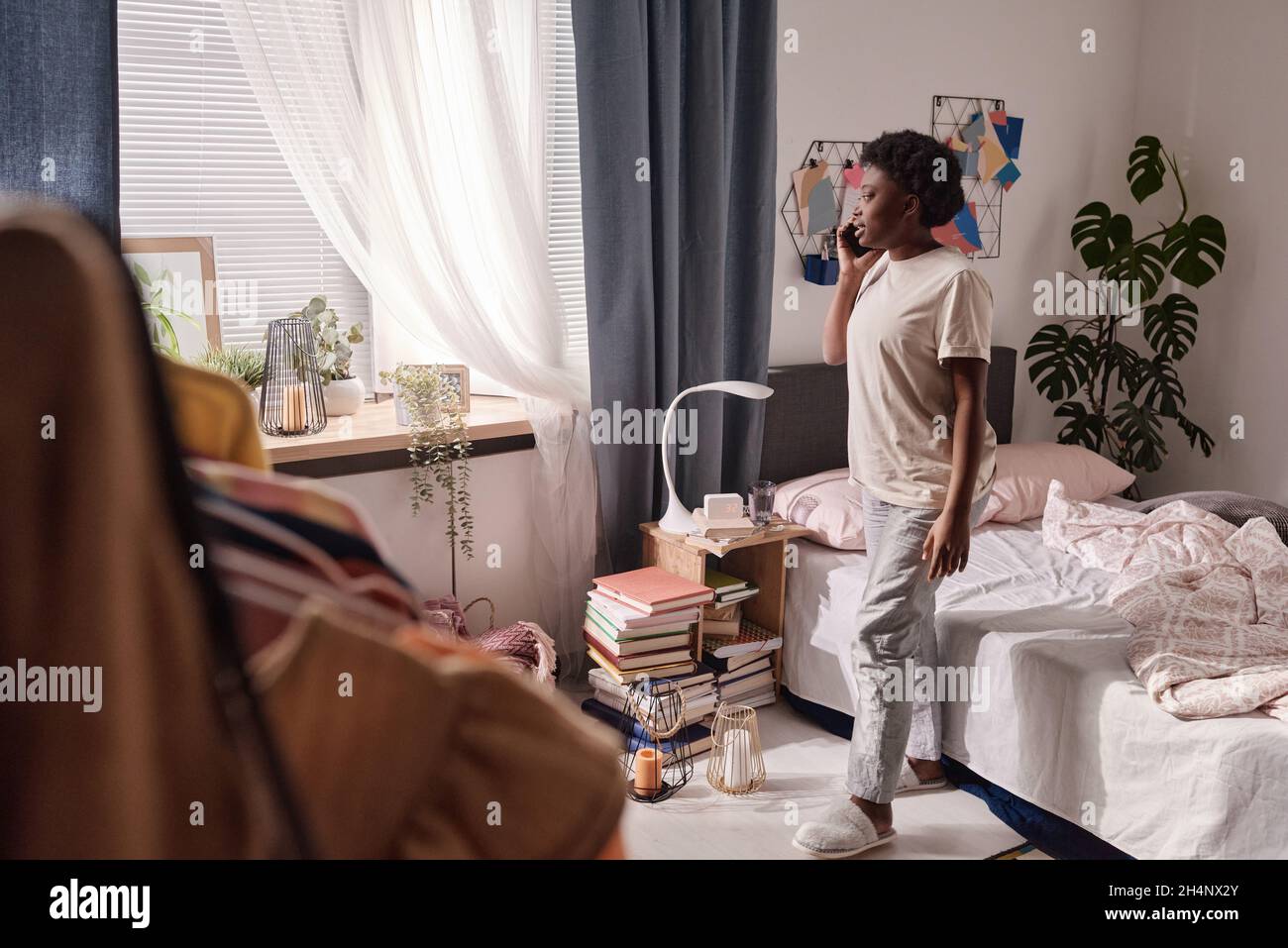 Afrikanische junge Frau, die auf ihrem Handy spricht, während sie um ihr Schlafzimmer geht Stockfoto