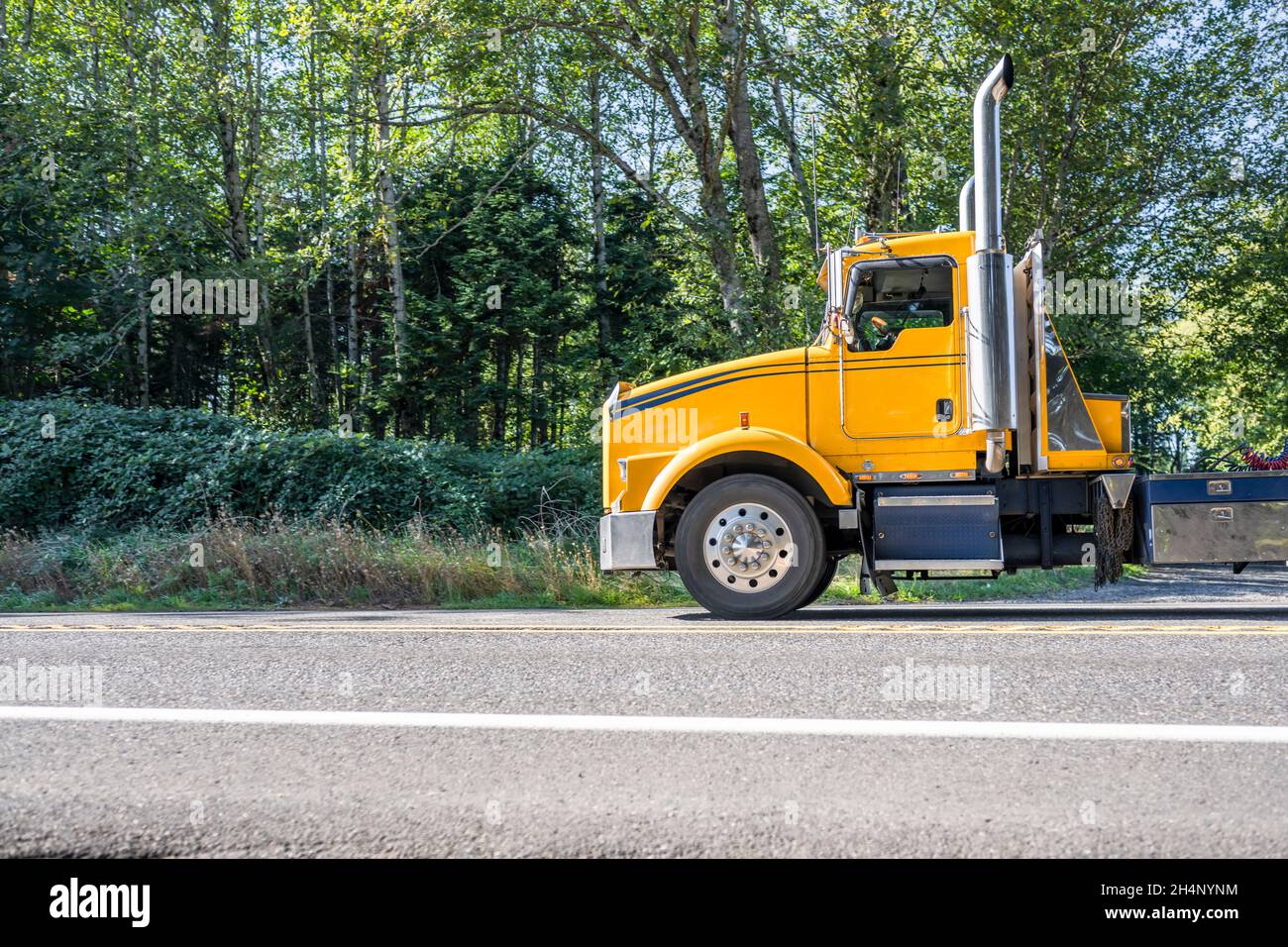 Leistungsstarke gelbe Big Rig klassischen Semi-Truck transportieren kommerzielle Fracht auf Flachbett-Sattelauflieger fahren auf der engen gewundenen Bergstraße mit aut Stockfoto