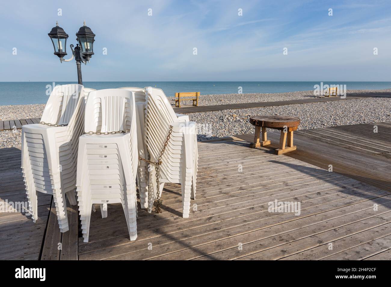 Stühle am Fuß eines Laternenpfades am Rande eines Kiesstrandes in Cayeux-sur-Mer gestapelt. Opal Coast, Frankreich Stockfoto