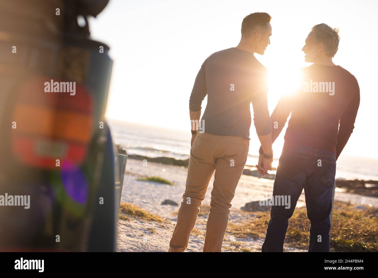 Glückliches kaukasisches, schwules, männliches Paar, das sich die Hände hielt und am Meer vom Auto weg ging Stockfoto