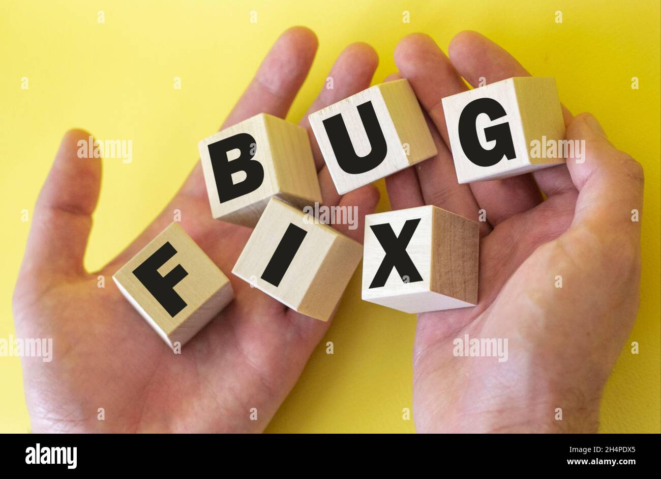 Bugfix, Text wird auf Holzklötze in männlichen Händen auf gelbem Hintergrund geschrieben Stockfoto