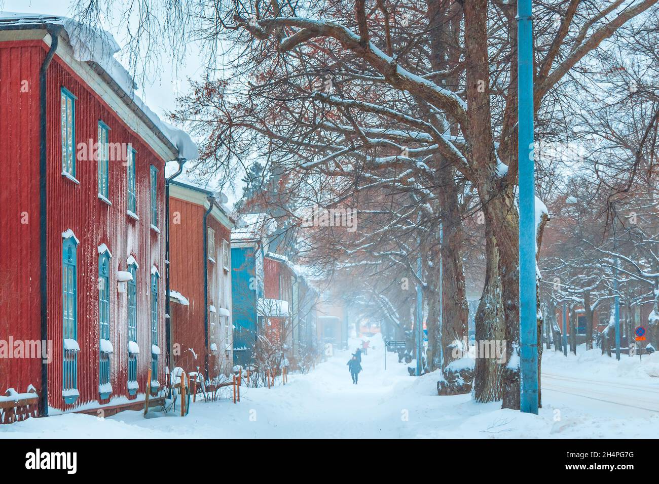 Winterschneesturm. Menschen gehen verschneite Straße mit alten bunten Häusern. Schneebedeckte Straße mit roten Gebäuden. Schneefall in der Stadt. Finnische Architektur. Stockfoto