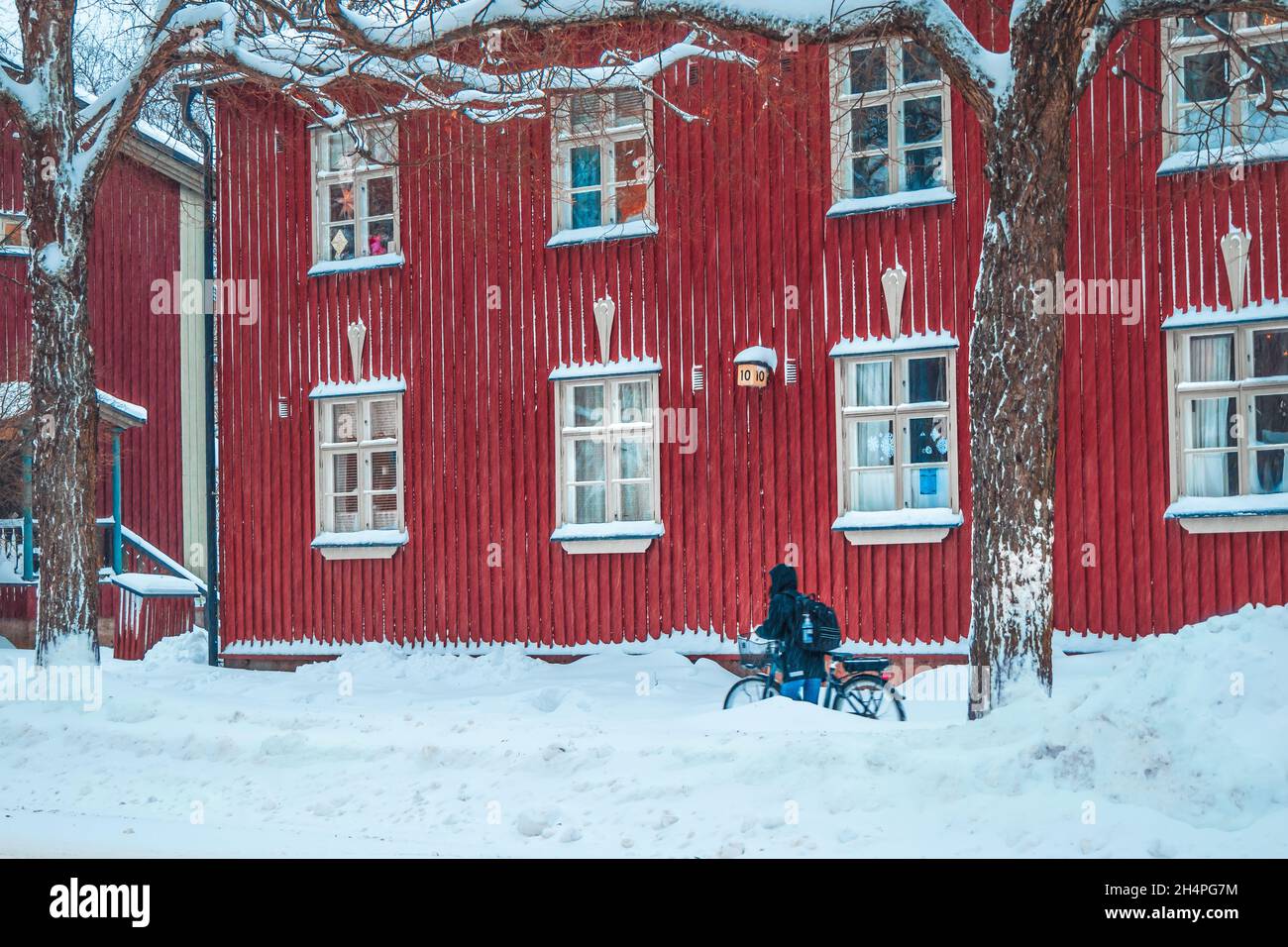 Ein Radfahrer schiebt ein Fahrrad durch den Schnee. Ein Biker mit Fahrrad an einer schneebedeckten Straße. Alte rote Holzhäuser in der Stadt in Finnland. Finnische Lebensart Stockfoto