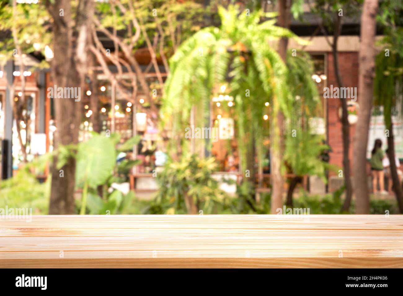 Warme Holztischplatte (Bar) mit Unschärfe auf grünen Palmenblättern oder Bäumen im tropischen Wald mit Bokeh-Licht im Hintergrund - Verwendung für Mock Up-Vorlage für di Stockfoto