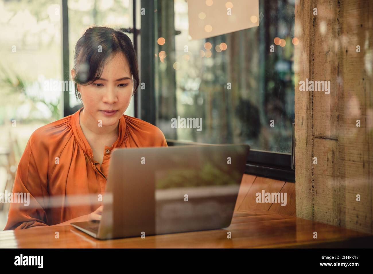 Asiatische Frau mit Laptop in Café-Café, warme Farbe. Freiberuflicher Mitarbeiter, der mit einem Laptop in einem Café arbeitet Stockfoto