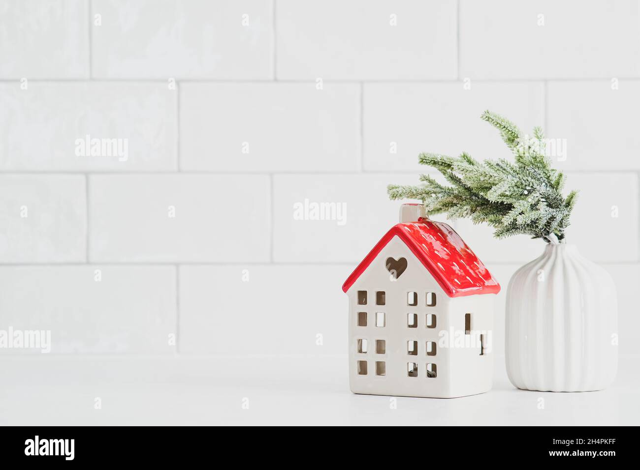 Nordische Weihnachtsdekoration auf Backsteinwand Hintergrund. Kleines Keramikhaus und Vase mit Tannenzweig. Gemütliches Zuhause, Hygge Winterurlaub Konzept. Stockfoto