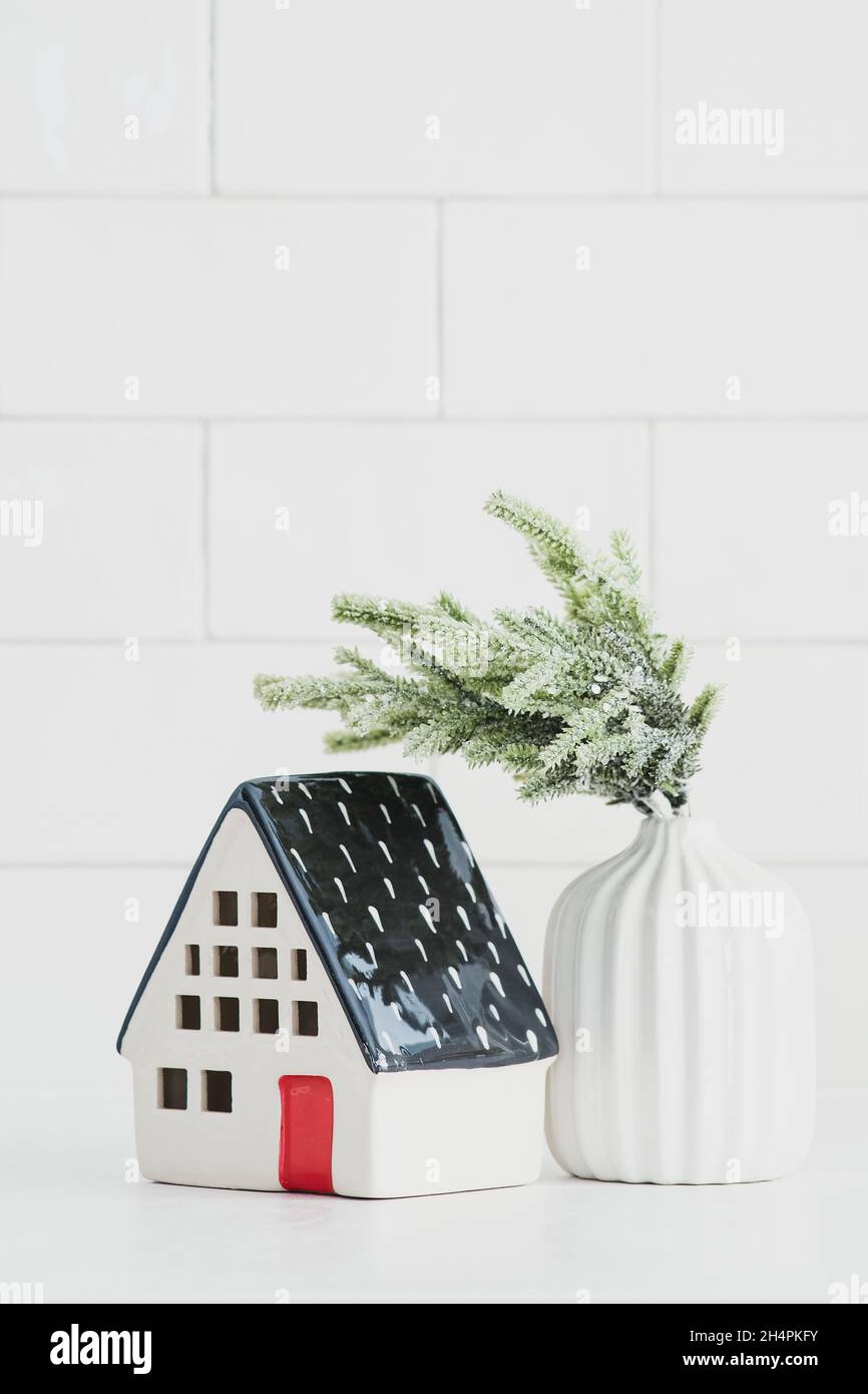 Nordisches Weihnachtsdekor. Kleines Keramikhaus und Vase mit Tannenzweig. Gemütliches Zuhause, Hygge, skandinavischer Stil. Stockfoto