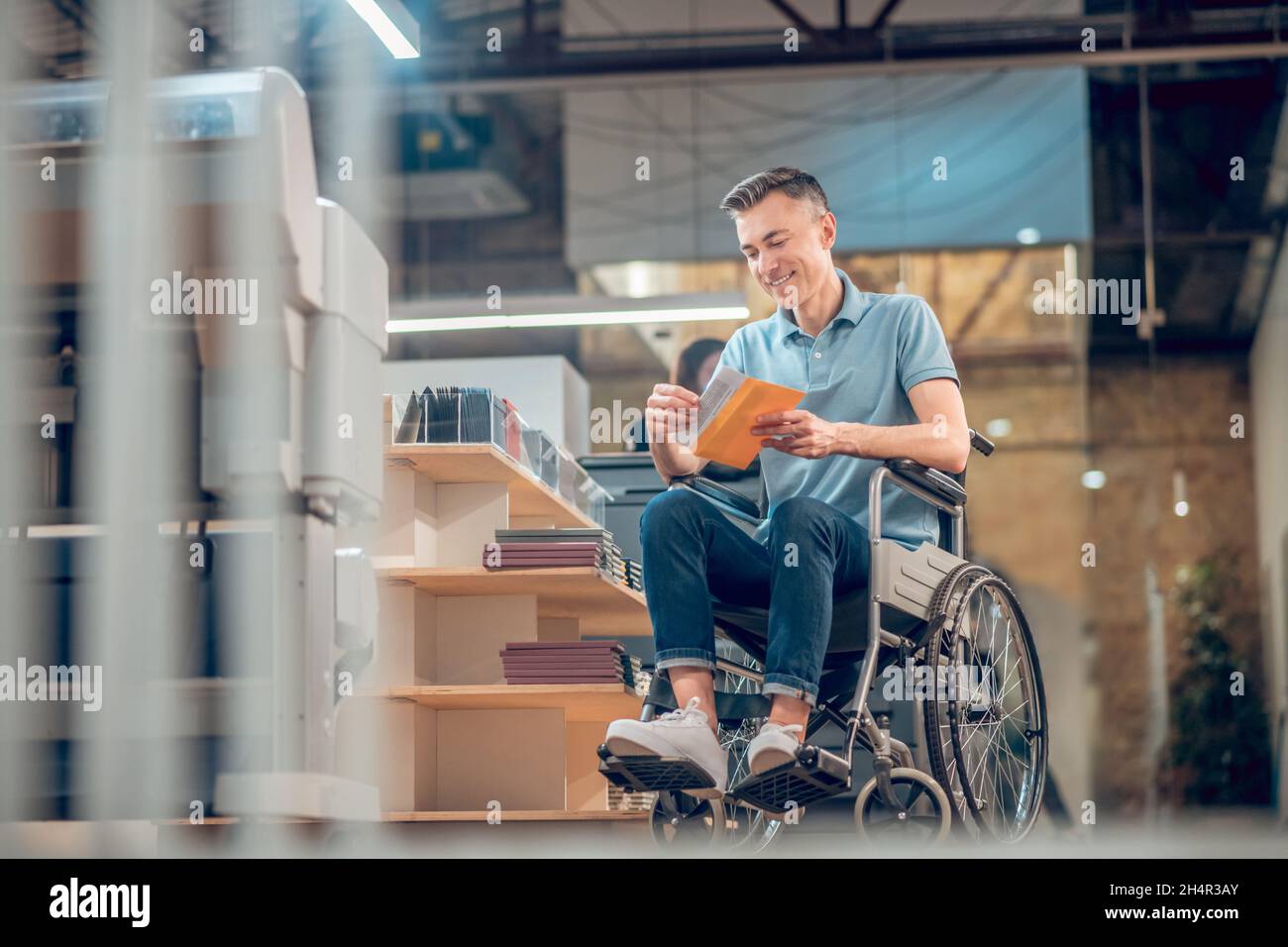 Glücklicher Mann im Rollstuhl, der Briefumschlag mit Postkarte ansah Stockfoto