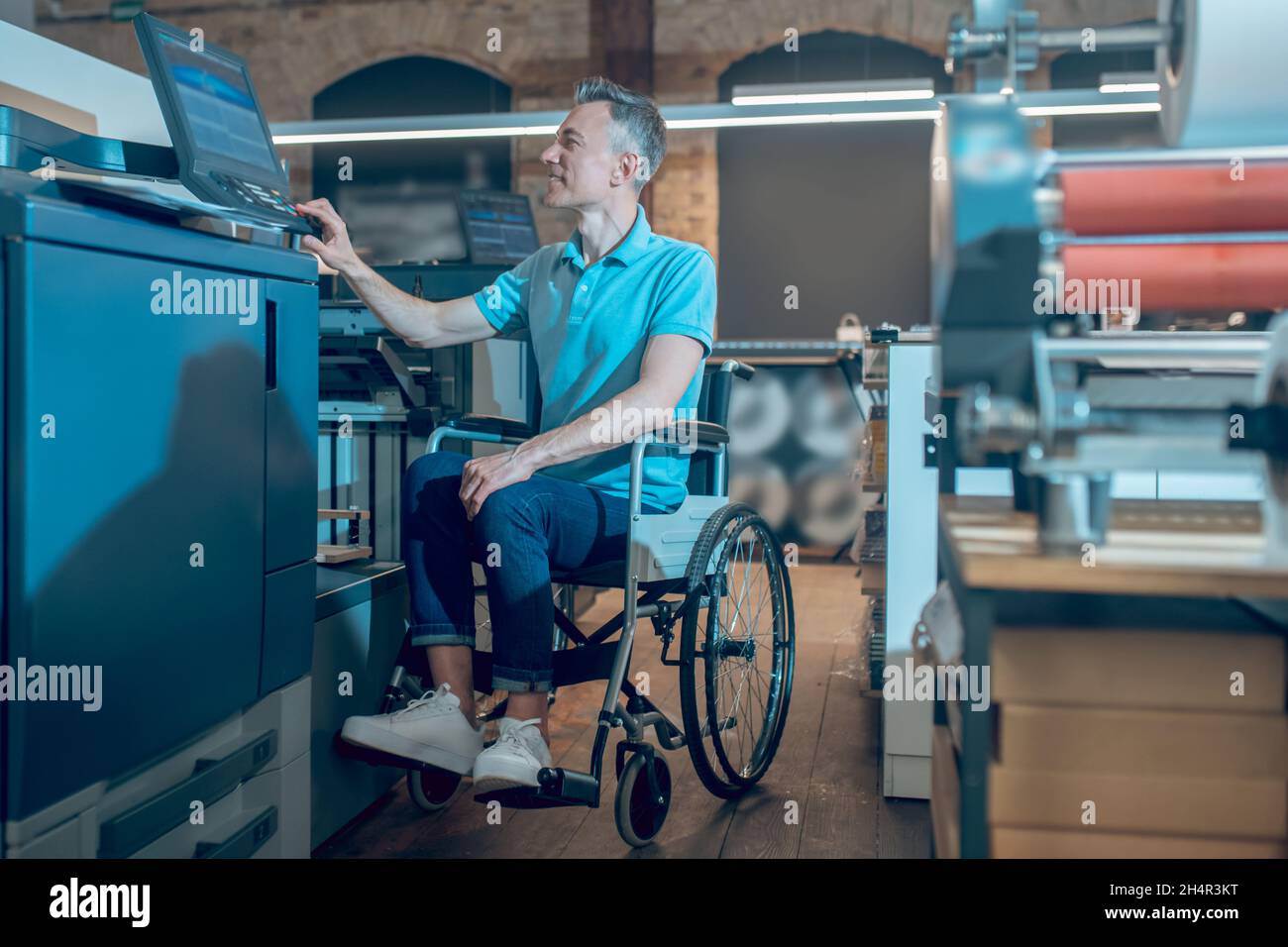 Mann im Rollstuhl, der die Bedienkonsole der Bürogeräte berührt Stockfoto