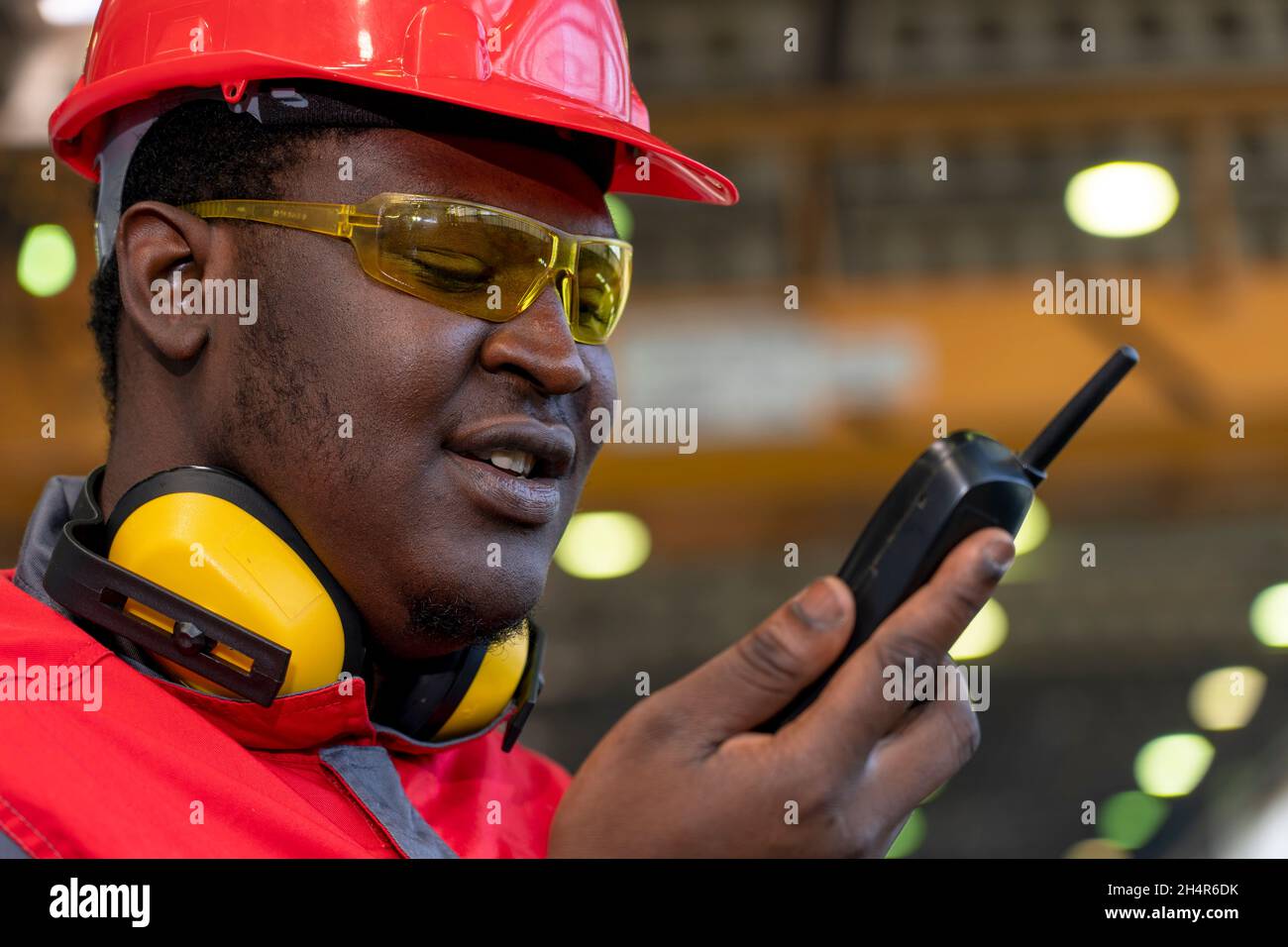 Portrait Eines Schwarzen Industriearbeiters In Rotem Helm, Gelber Schutzbrille, Gehörschutzausrüstung Und Arbeitskleidung. Stockfoto