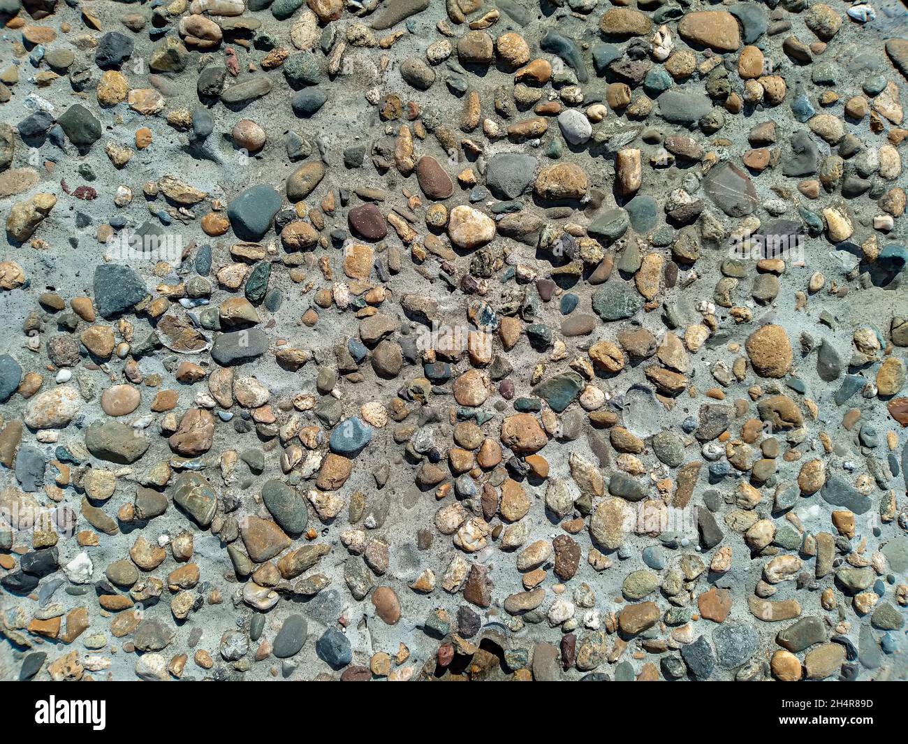 Betonoberfläche von Groyne mit farbigen Kiessteinen aus dem Meer in verschiedenen Formen, Hintergrund Stockfoto