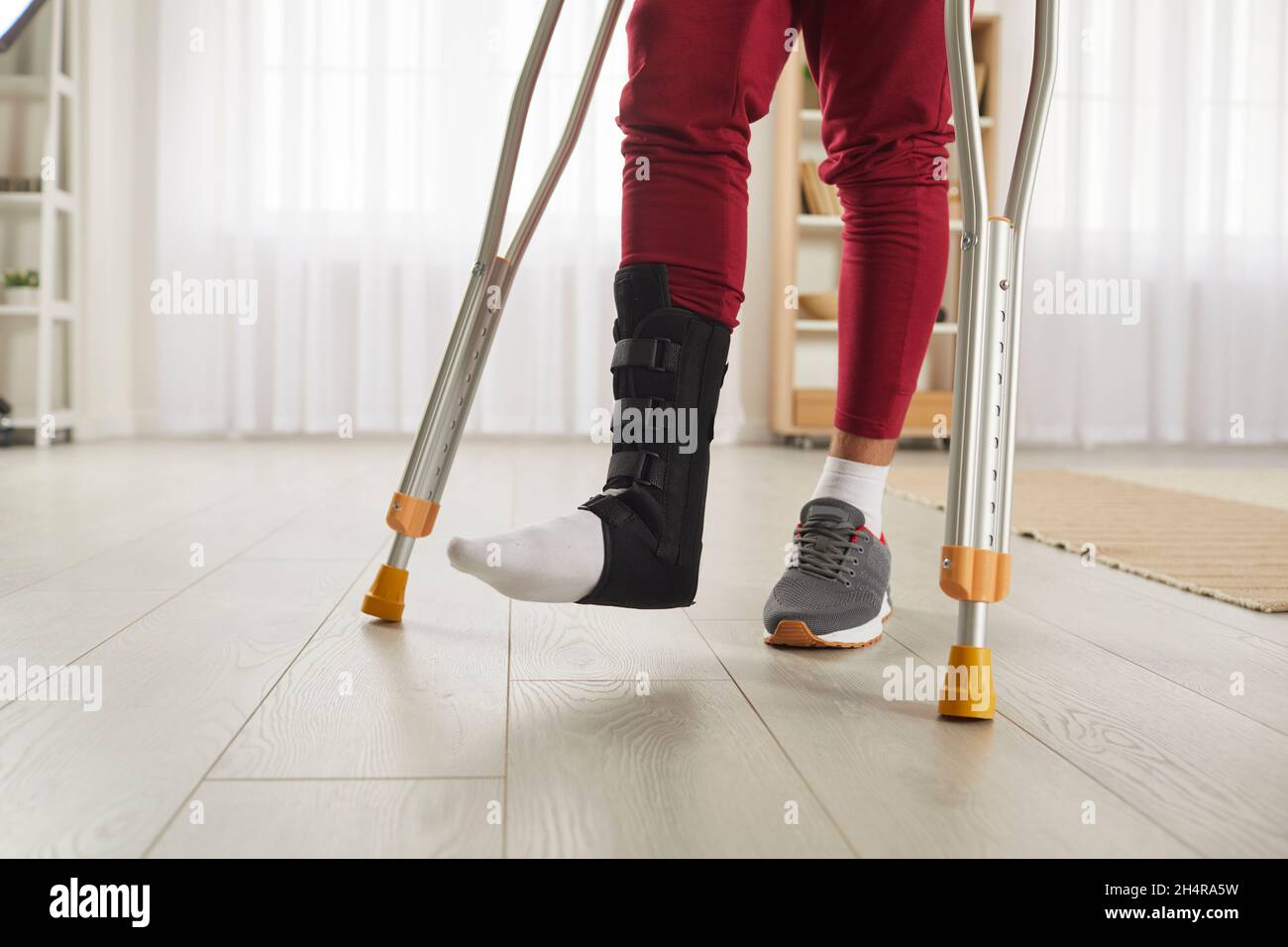 Person mit Fußverletzung, die Beinstützen trägt und zu Hause auf Krücken läuft Stockfoto