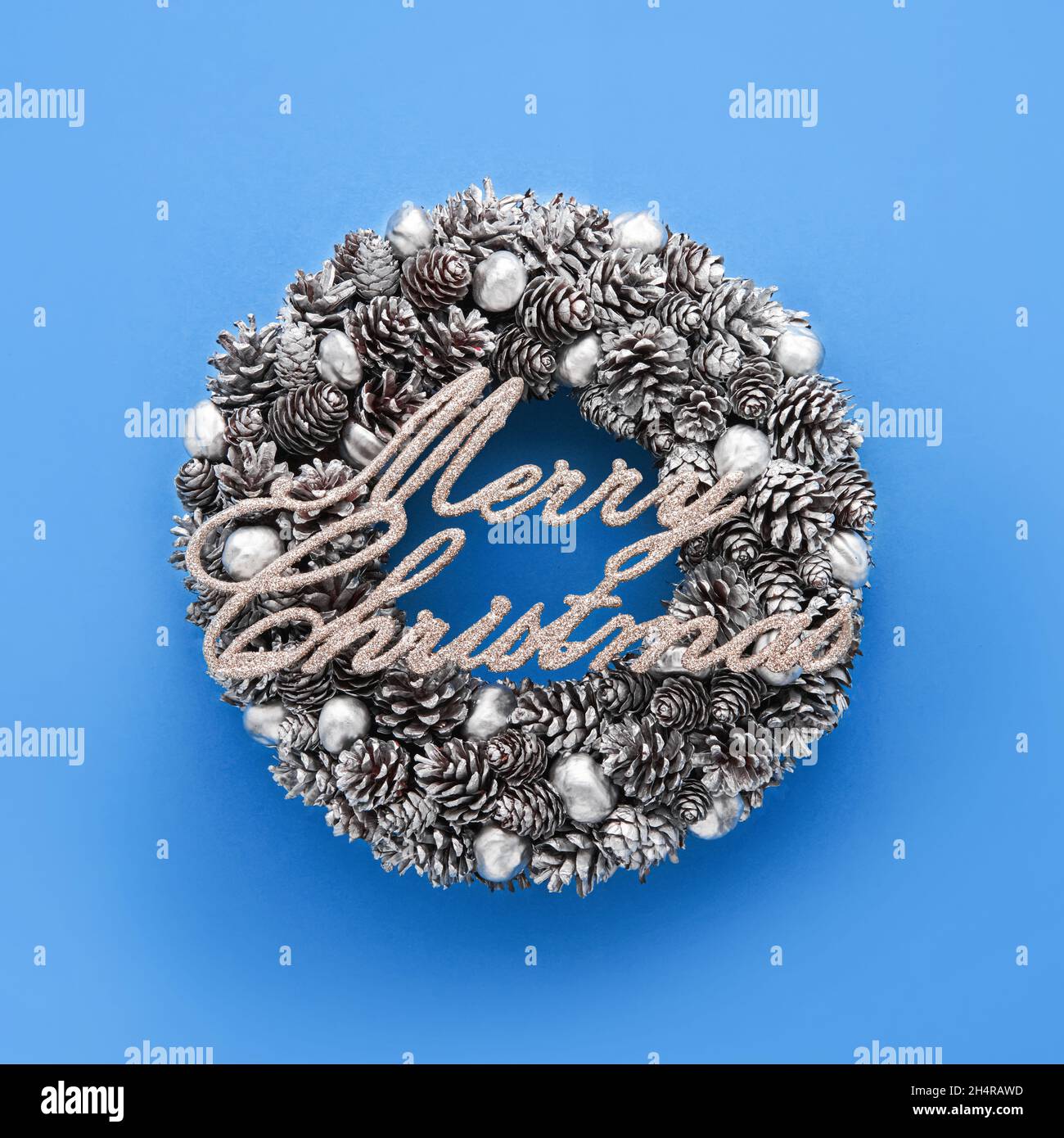 Silber Text Frohe Weihnachten auf einem silbernen Weihnachtskranz auf blauem Hintergrund. Draufsicht, Kopierbereich Stockfoto