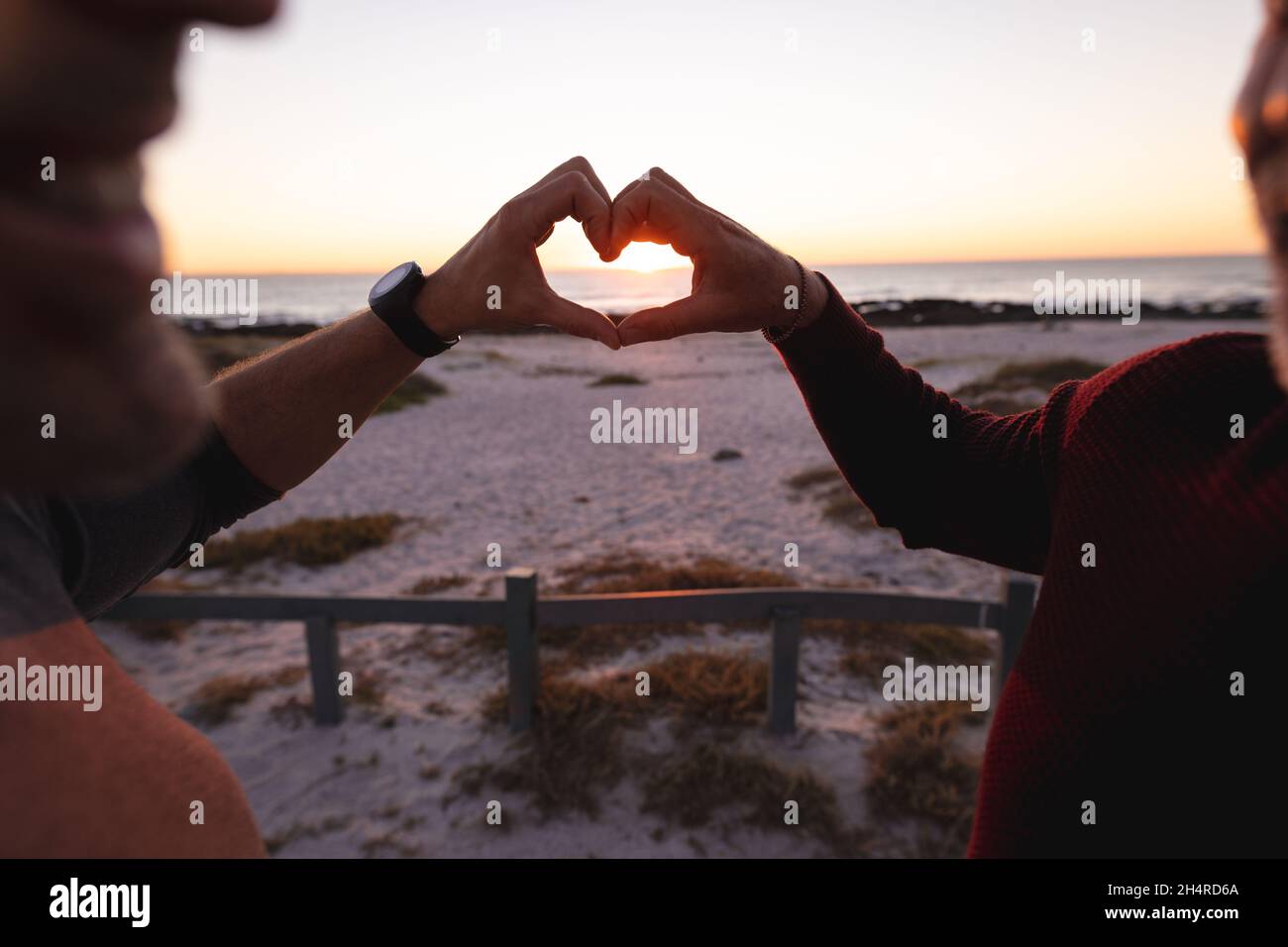 Glücklich kaukasisch Gay Männlich Paar bilden Herzform mit Händen am Strand bei Sonnenuntergang Stockfoto