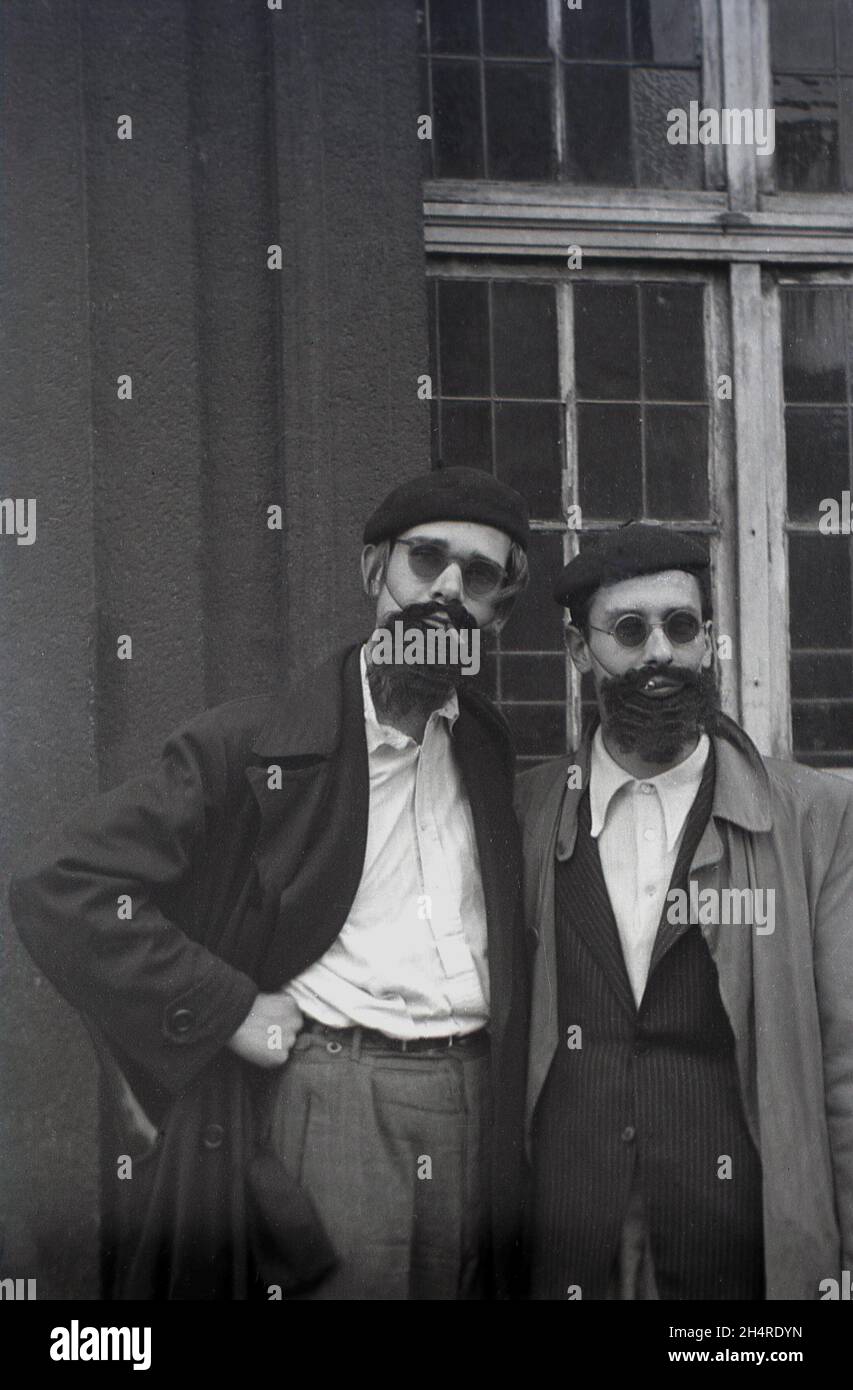 In den 1960er Jahren, historisch, zwei Männer, die vor einem Gebäude in Regenmänteln standen und mit Baretten, Sonnenbrillen und falschen Bärten verkleidet waren, plus rauchenden kleinen Zigarren, Deutschland. Stockfoto