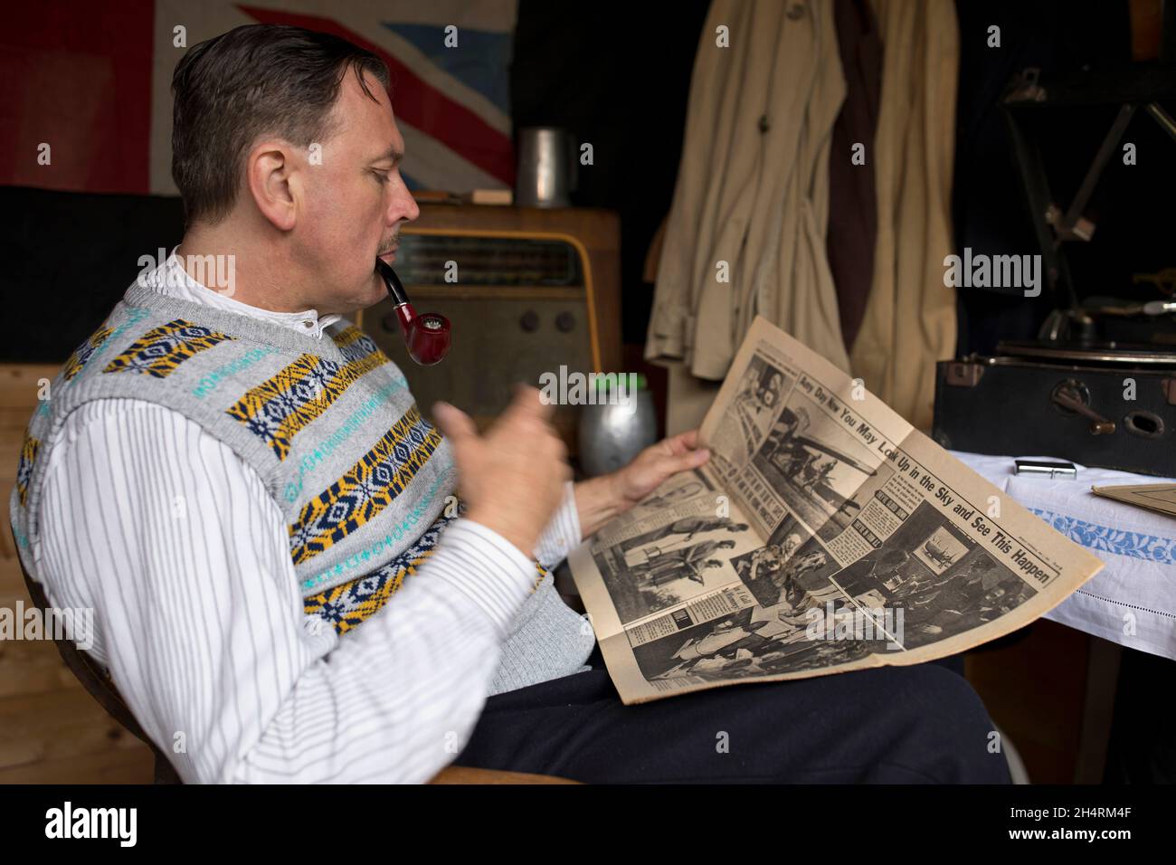 Großbritannien der 1940er Jahre: Mann raucht Pfeife, liest Zeitung, während er auf Schallplatte zugehört. Stockfoto