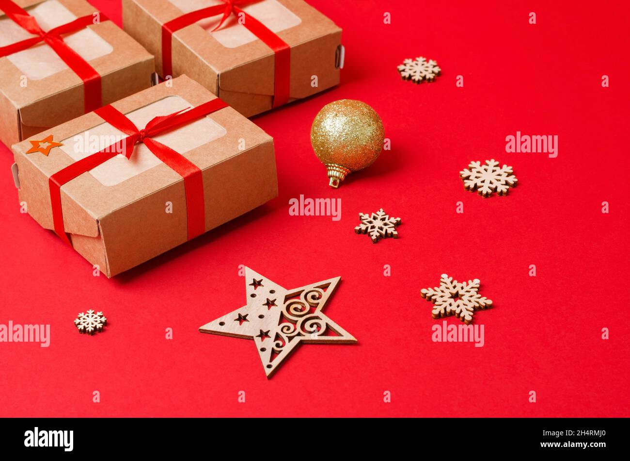 Bastelkisten und dekorative Weihnachtsbaumspielzeug aus Holz auf rotem Hintergrund. Weihnachten Hintergrund. Weihnachten, Neujahrsgeschenke aus Öko-Material Stockfoto