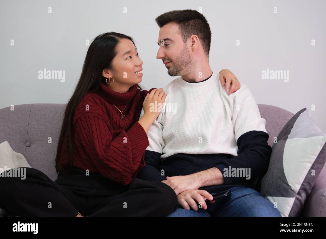 Junges Paar, das sich mit einem Laptop auf der Couch zu Hause entspannt und lächelt. Stockfoto